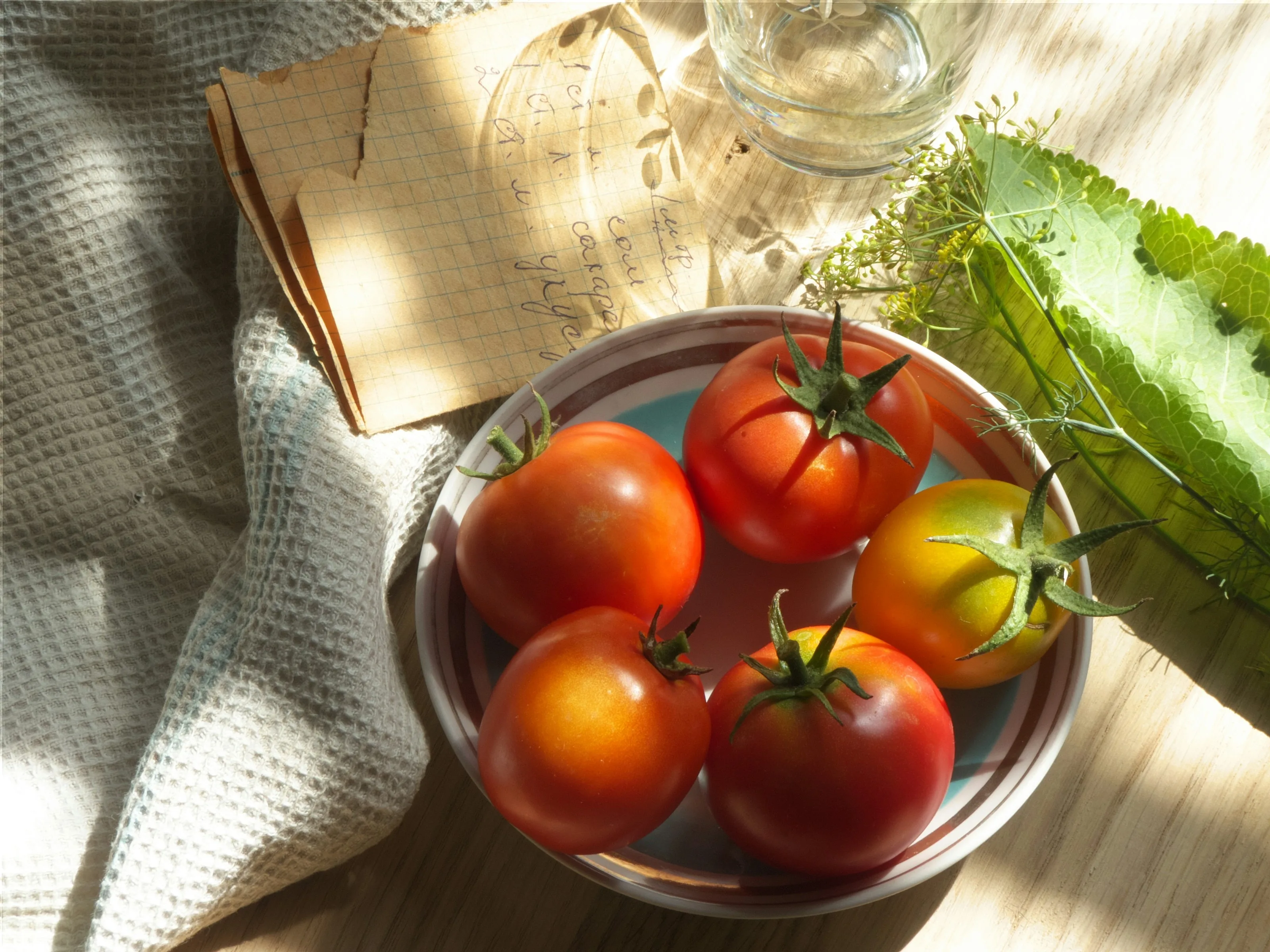 A bowl of ripe tomatoes on linen in morning light