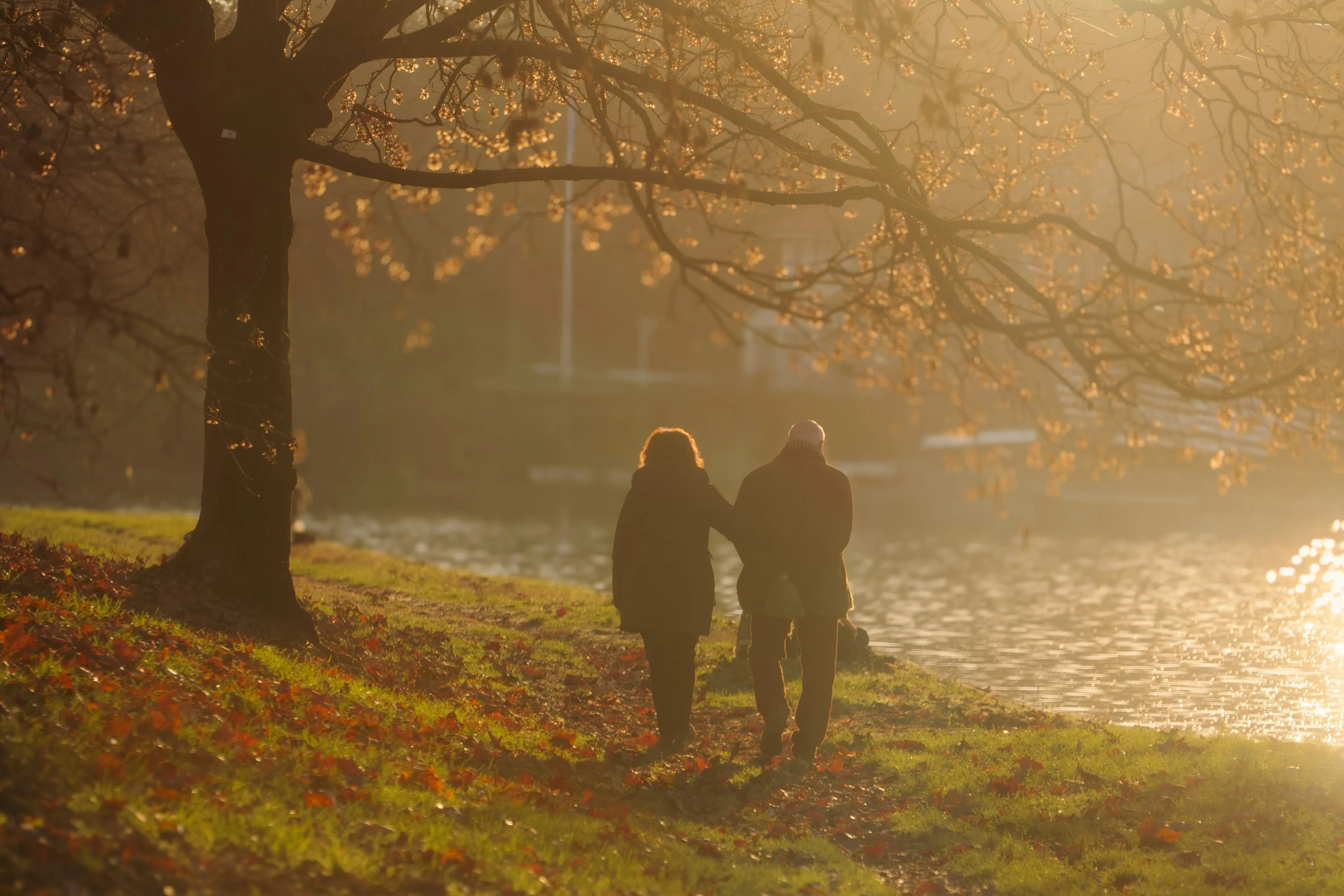 An older couple walking arm in arm along a river at sunset