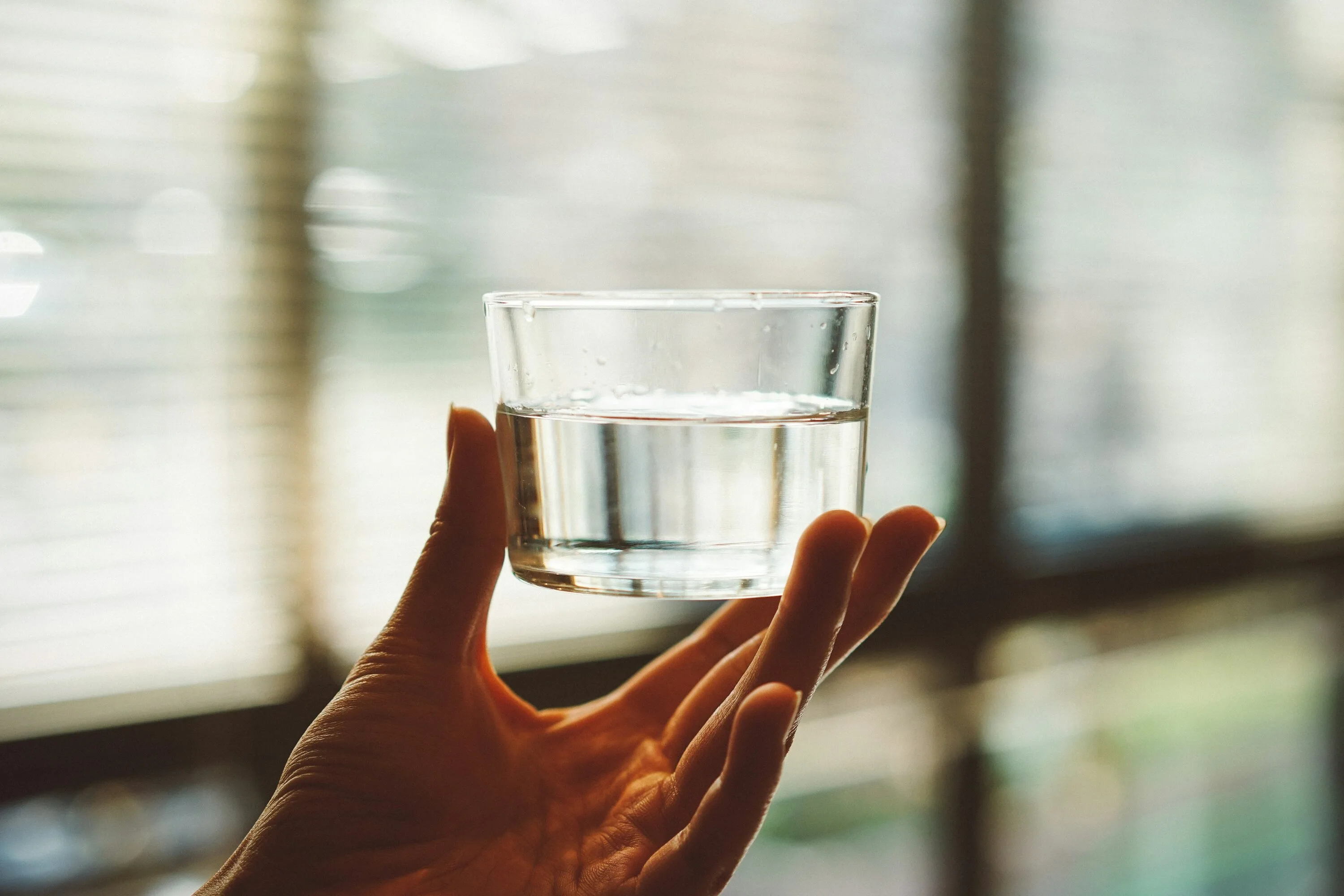 A hand holding a glass of water in soft window light